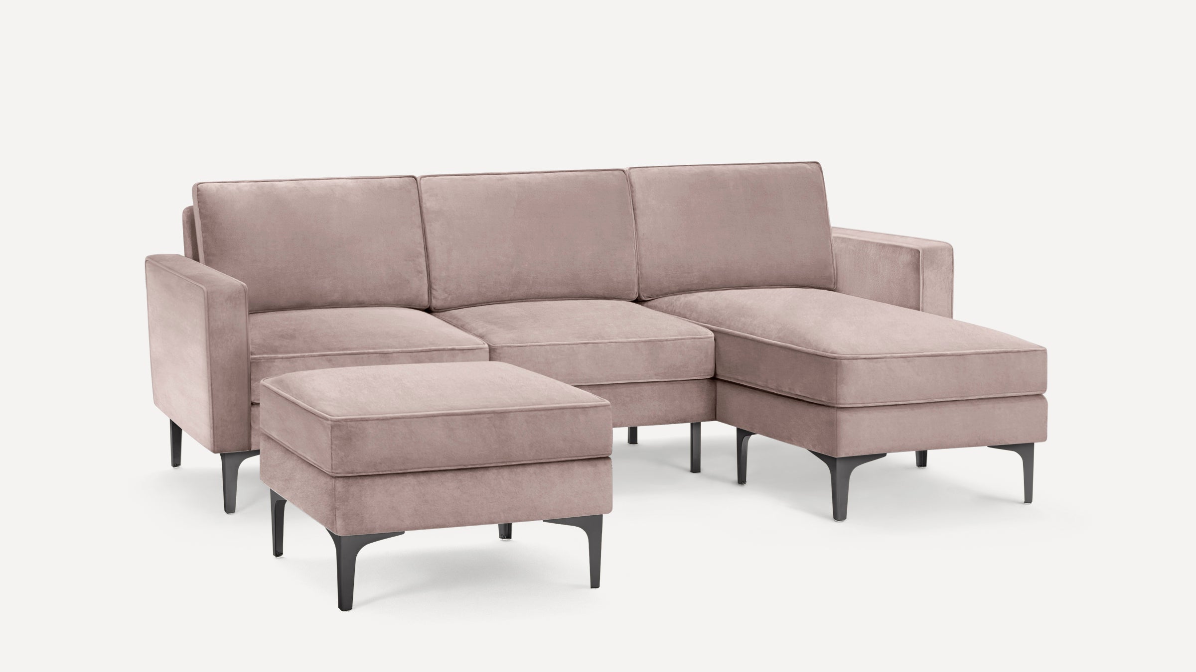 Modern sectional sofa with chaise lounge and matching ottoman, upholstered in soft dusty pink fabric with black tapered legs.