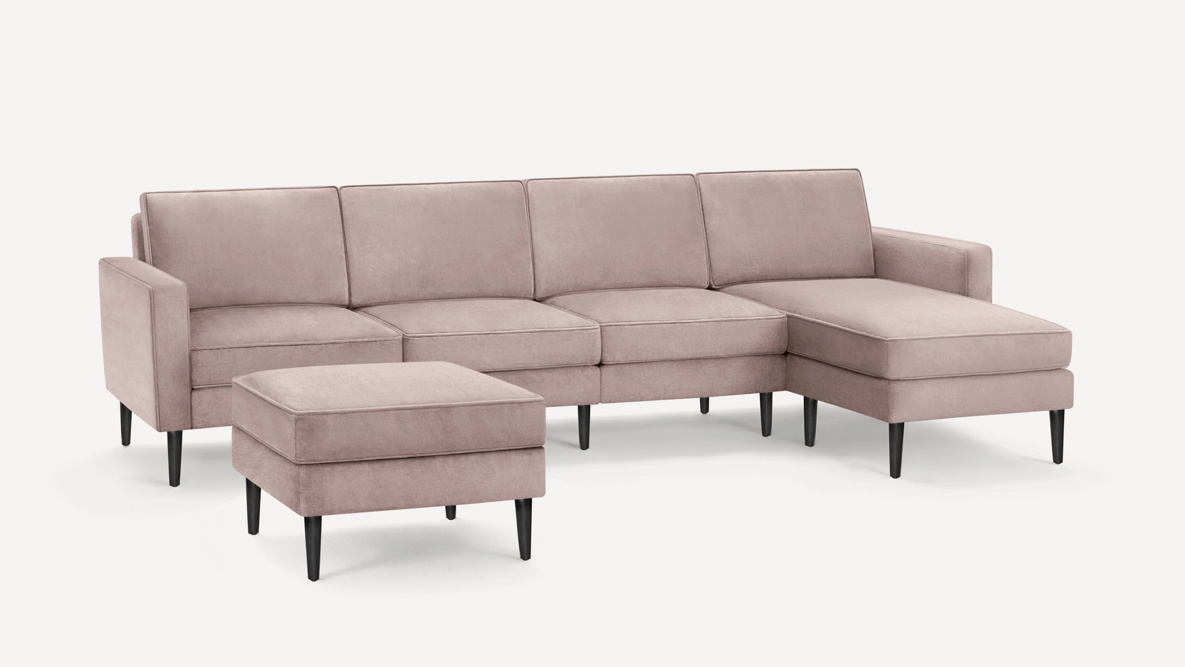 Light pink sectional sofa with chaise lounge and matching ottoman, featuring sleek black tapered legs and modern design.