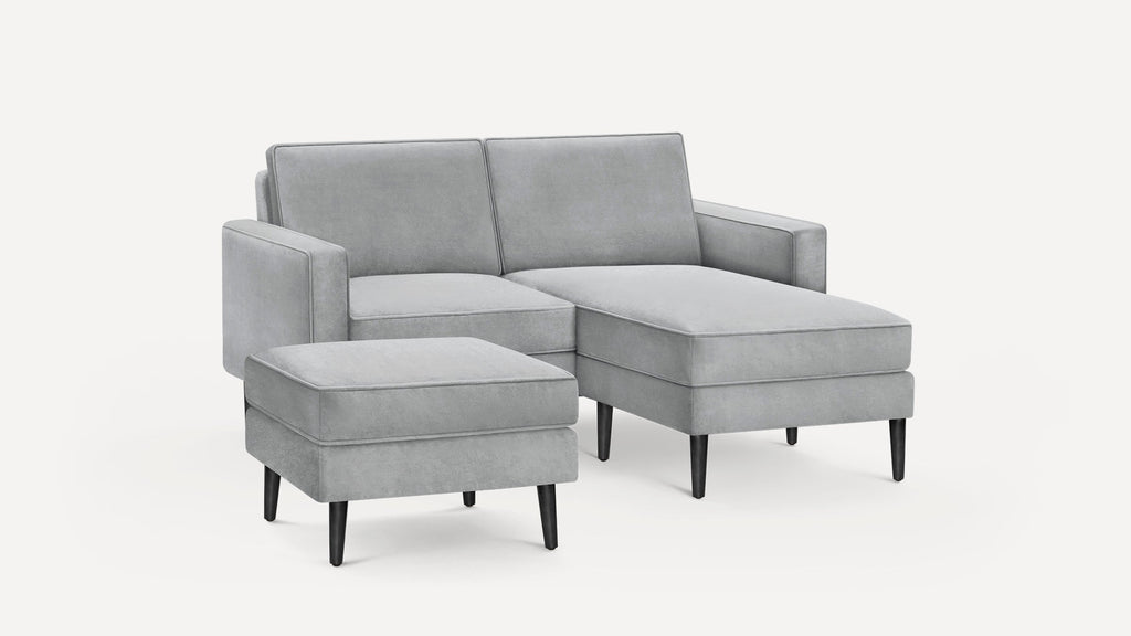 Modern light gray velvet sectional sofa with chaise lounge and matching ottoman, featuring black tapered legs.