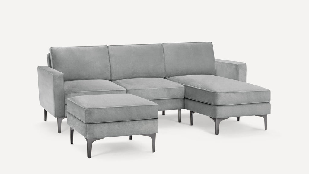 Modern gray velvet sectional sofa with chaise lounge and separate ottoman, featuring sleek black metal legs.