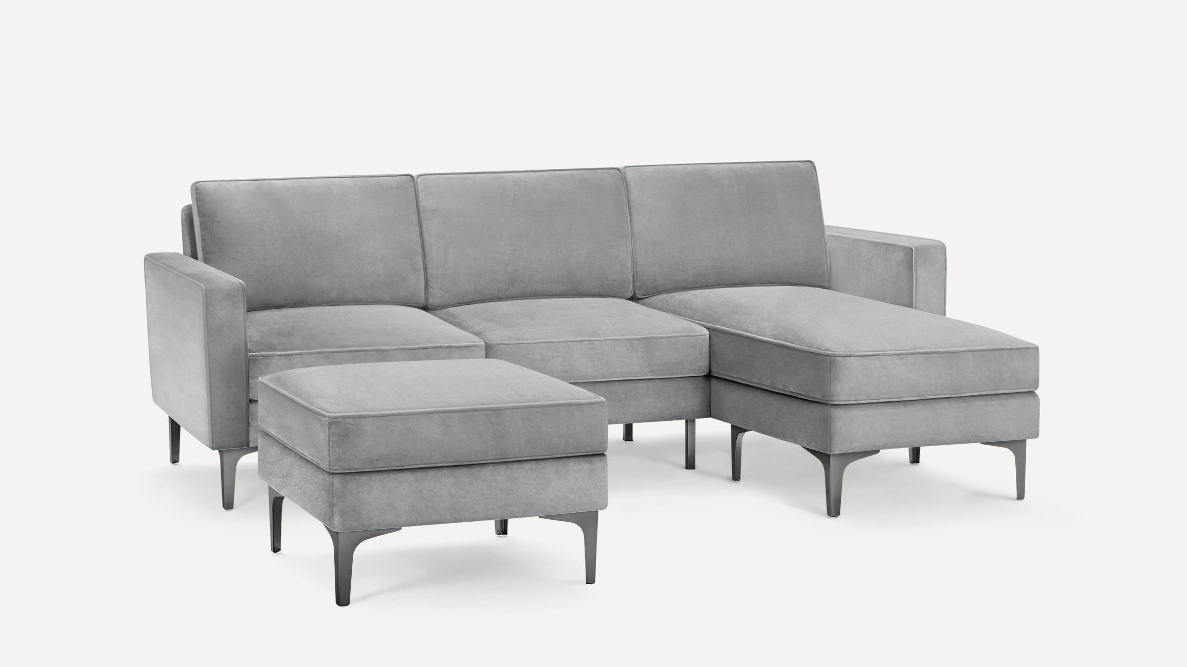 Modern gray velvet sectional sofa with chaise lounge and separate ottoman, featuring sleek black metal legs.