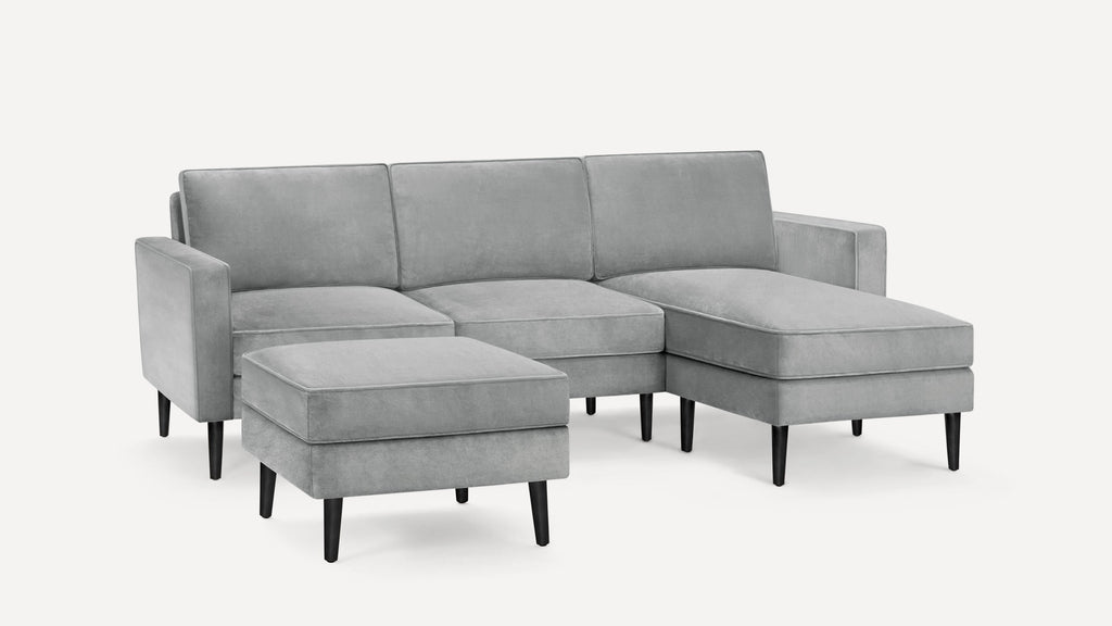 Modern light gray sectional sofa with chaise lounge and matching ottoman, featuring sleek black wooden legs.