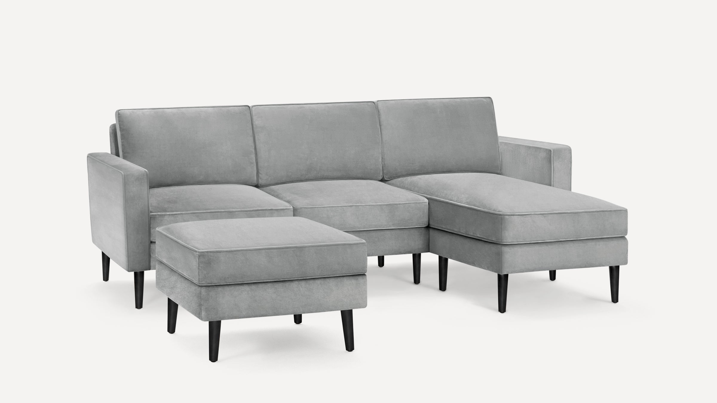 Modern light gray sectional sofa with chaise lounge and matching ottoman, featuring sleek black wooden legs.