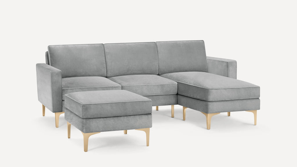 Gray sectional sofa with a cushioned ottoman, gold metal legs, and a modern minimalist design on a white background.