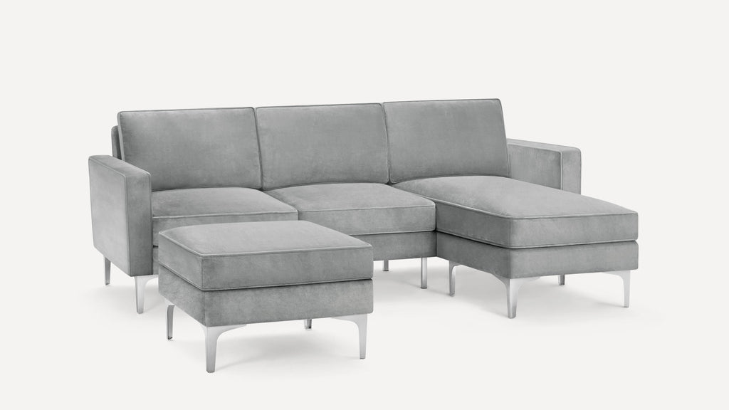 Modern sectional sofa with light gray upholstery, metal legs, and a matching ottoman, featuring a chaise lounge on the right side.