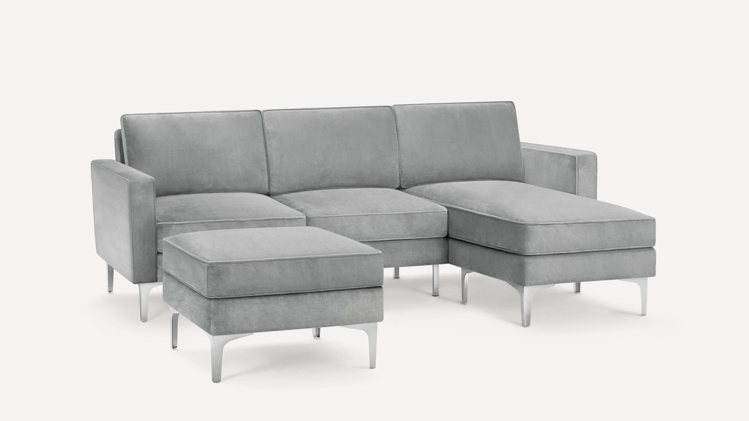 Modern sectional sofa with light gray upholstery, metal legs, and a matching ottoman, featuring a chaise lounge on the right side.