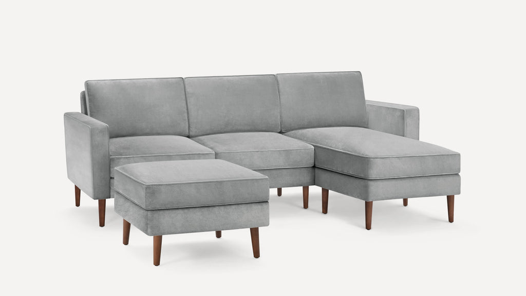 Light gray sectional sofa with wooden legs and matching ottoman, featuring clean, modern lines and plush cushions.