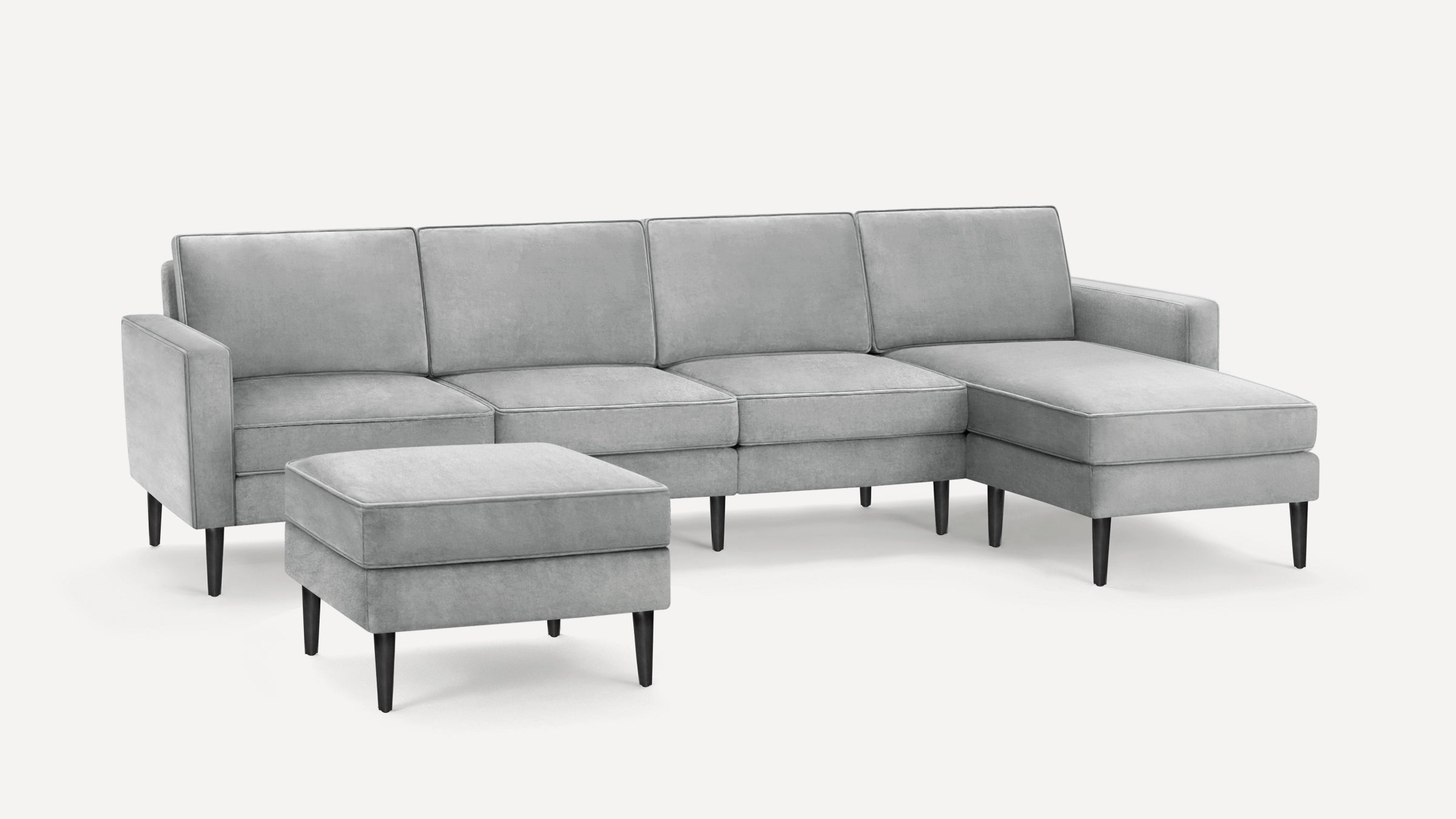 Light grey upholstered sectional sofa with chaise lounge and matching ottoman, featuring sleek black tapered legs.