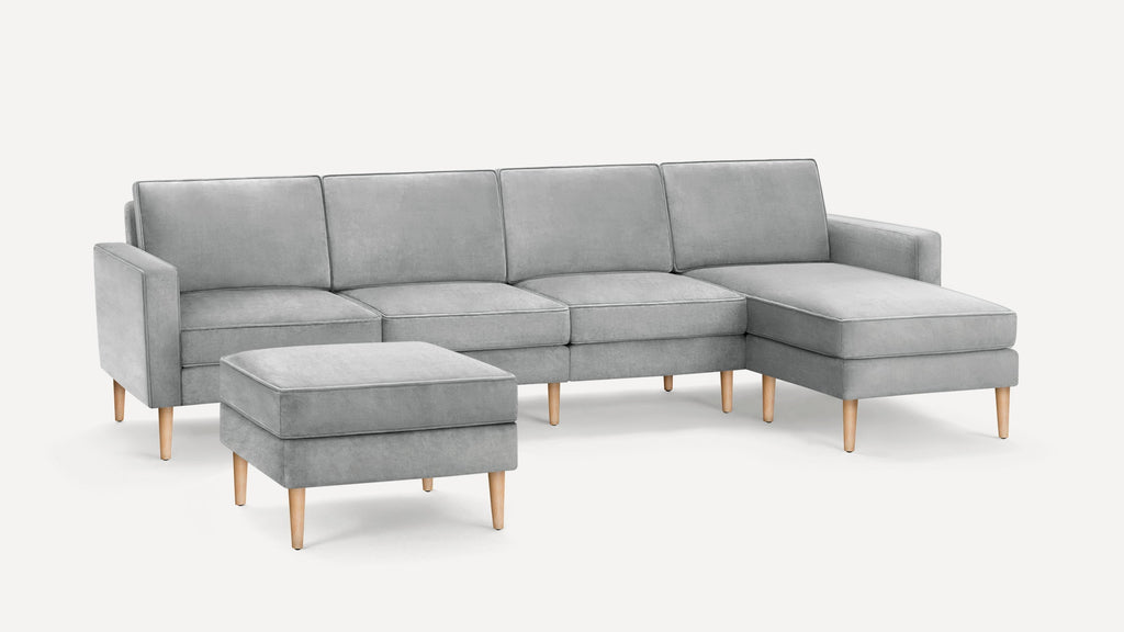 Light gray upholstered sectional sofa with wooden legs, featuring a chaise lounge and matching ottoman.