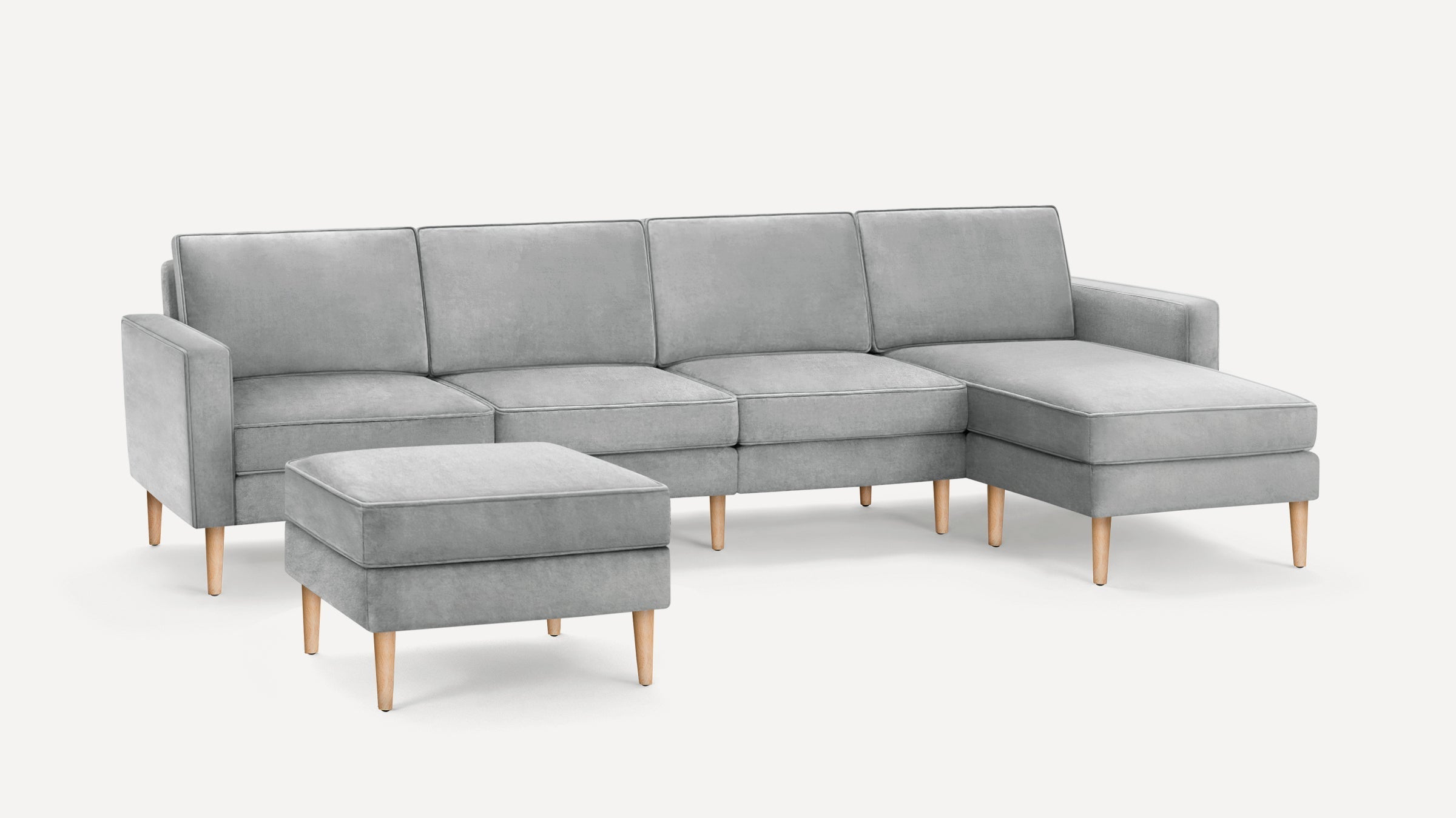 Light gray upholstered sectional sofa with wooden legs, featuring a chaise lounge and matching ottoman.