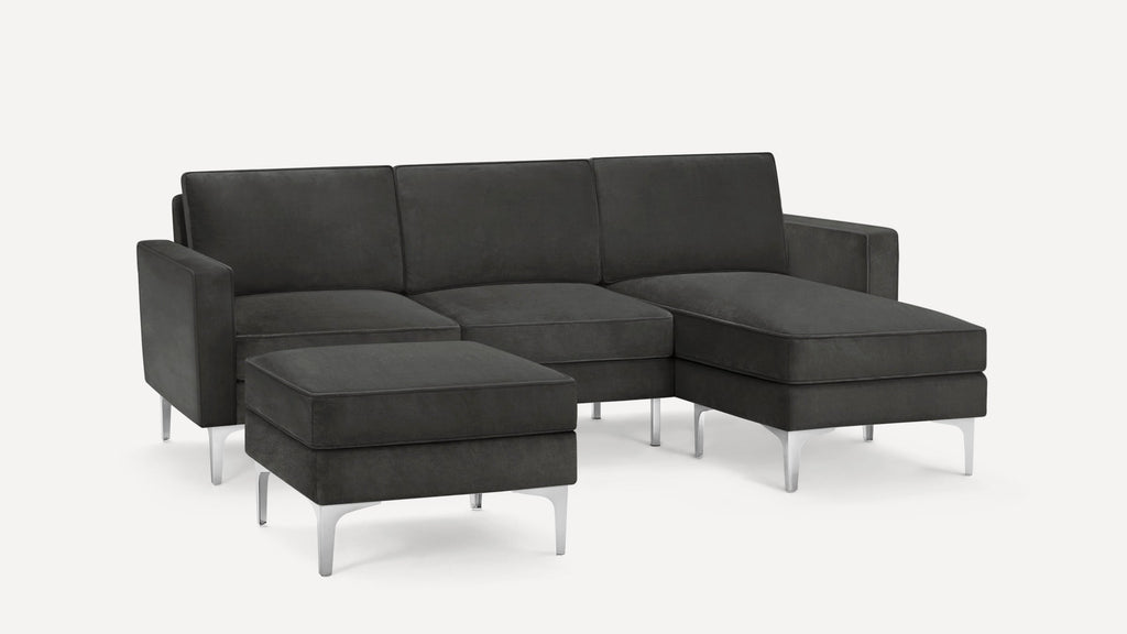 Modern dark gray sectional sofa with chrome metal legs and matching ottoman, featuring clean lines and plush cushions.