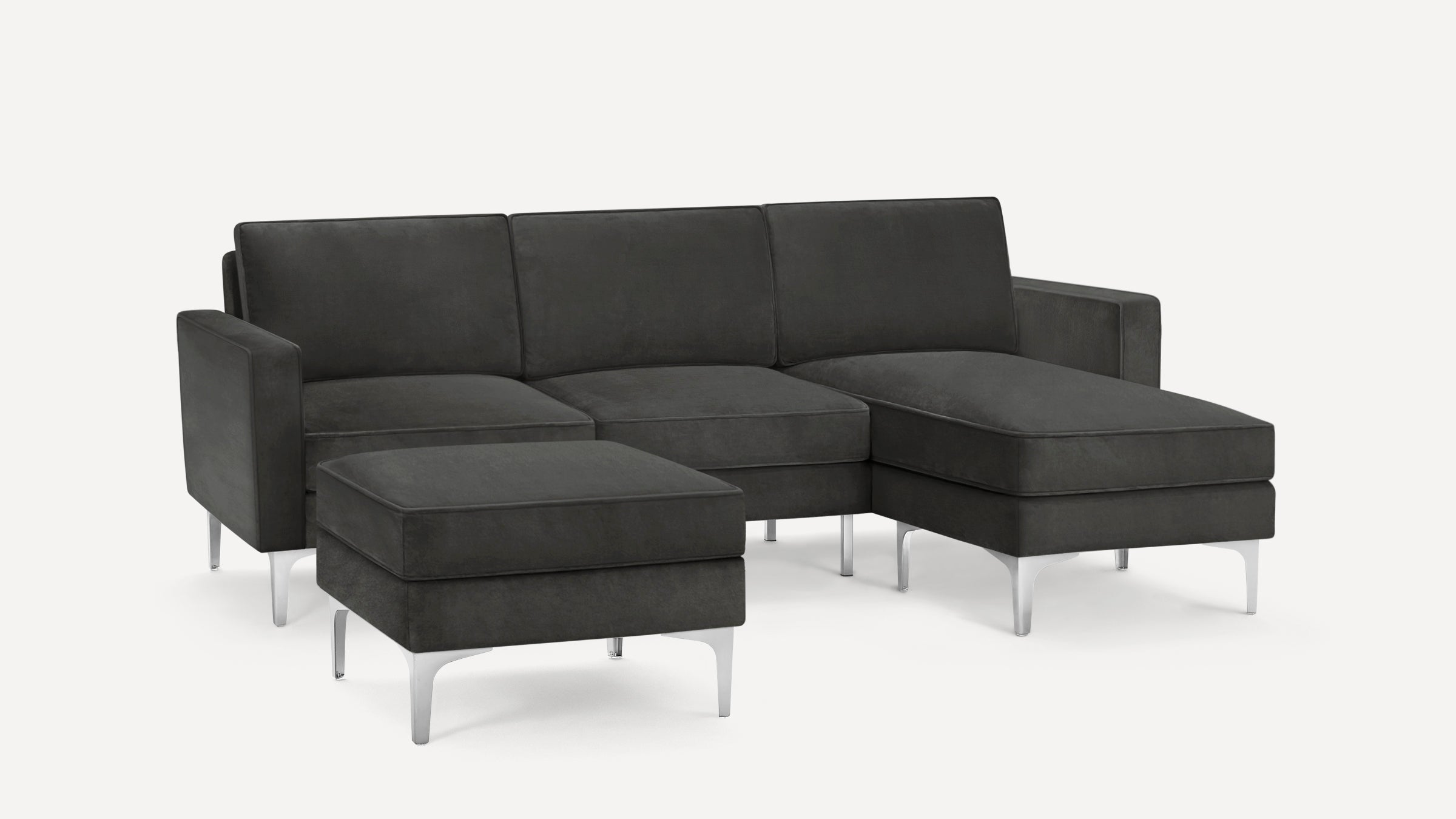 Modern dark gray sectional sofa with chrome metal legs and matching ottoman, featuring clean lines and plush cushions.