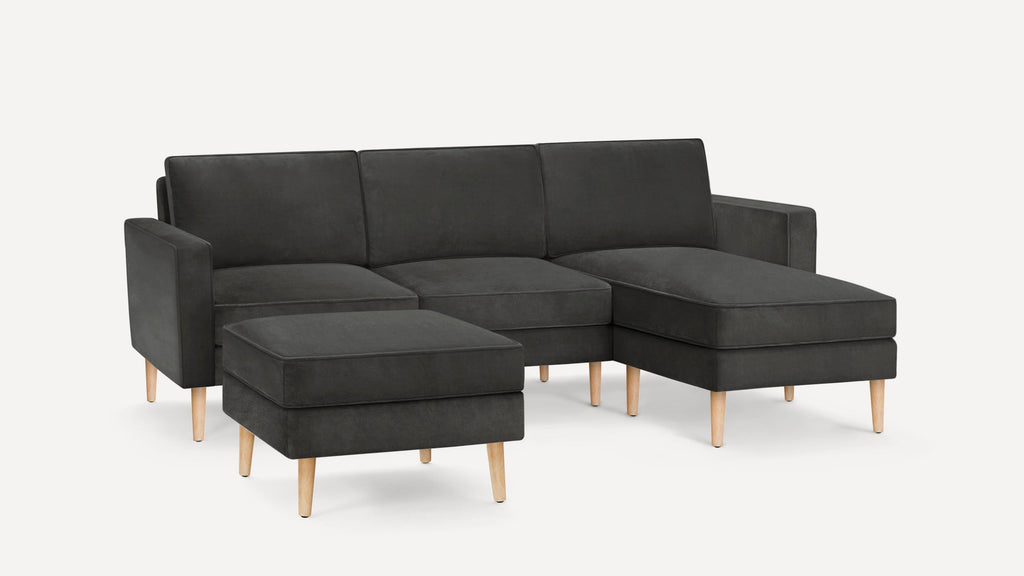 Dark gray sectional sofa with wooden legs and a matching ottoman on a plain white background.