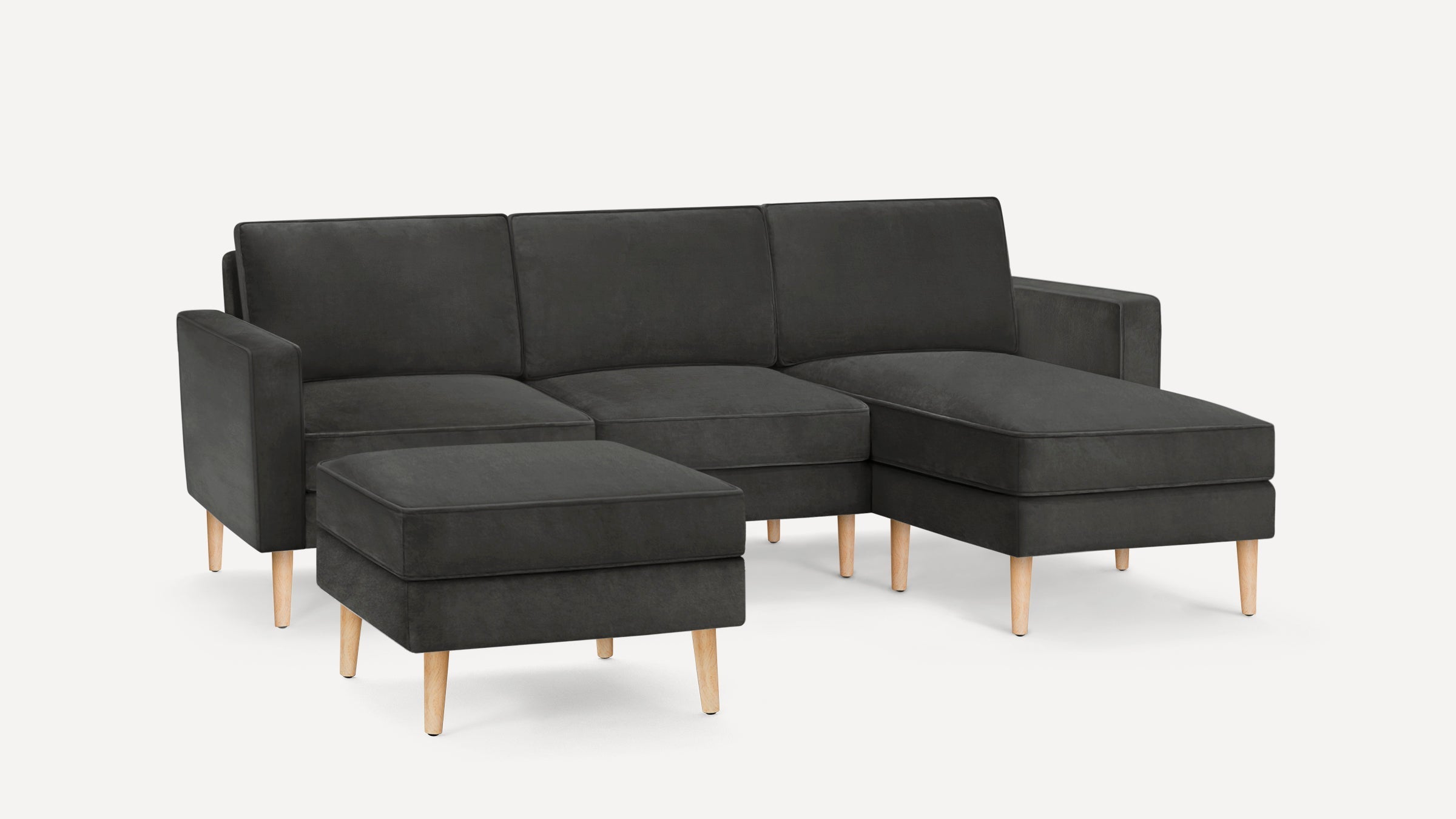 Dark gray sectional sofa with wooden legs and a matching ottoman on a plain white background.