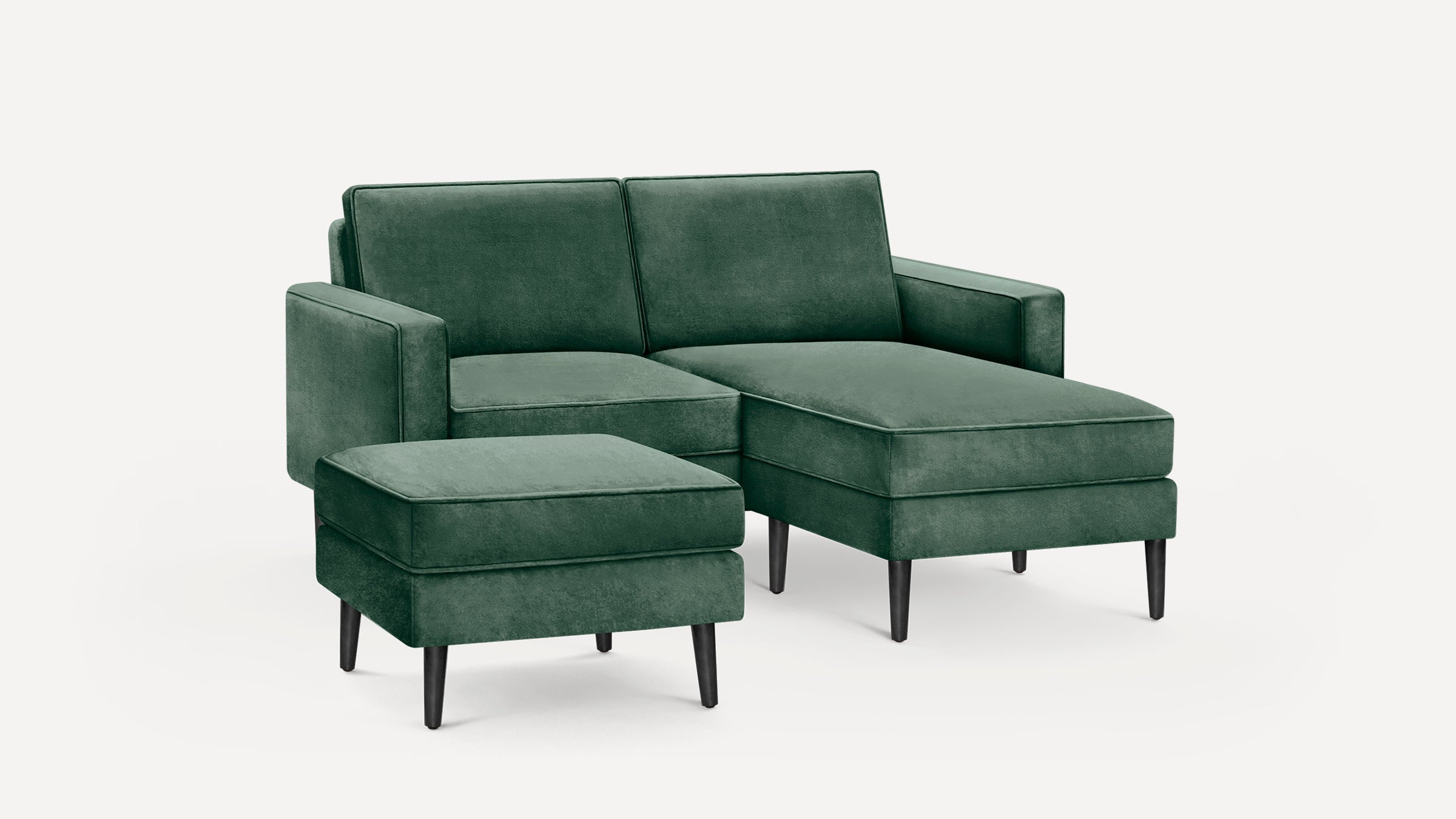Dark green velvet L-shaped sectional sofa with matching ottoman and black tapered legs on a white background.