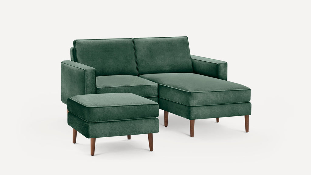Modern green velvet sectional sofa with matching ottoman, wooden tapered legs, clean lines, and plush cushions.