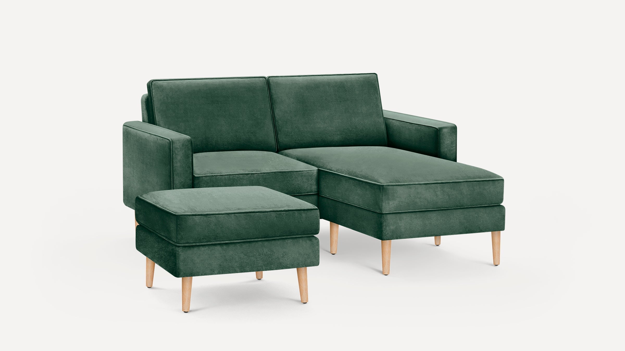 Green velvet sectional sofa with chaise lounge and matching ottoman, supported by light wooden legs.