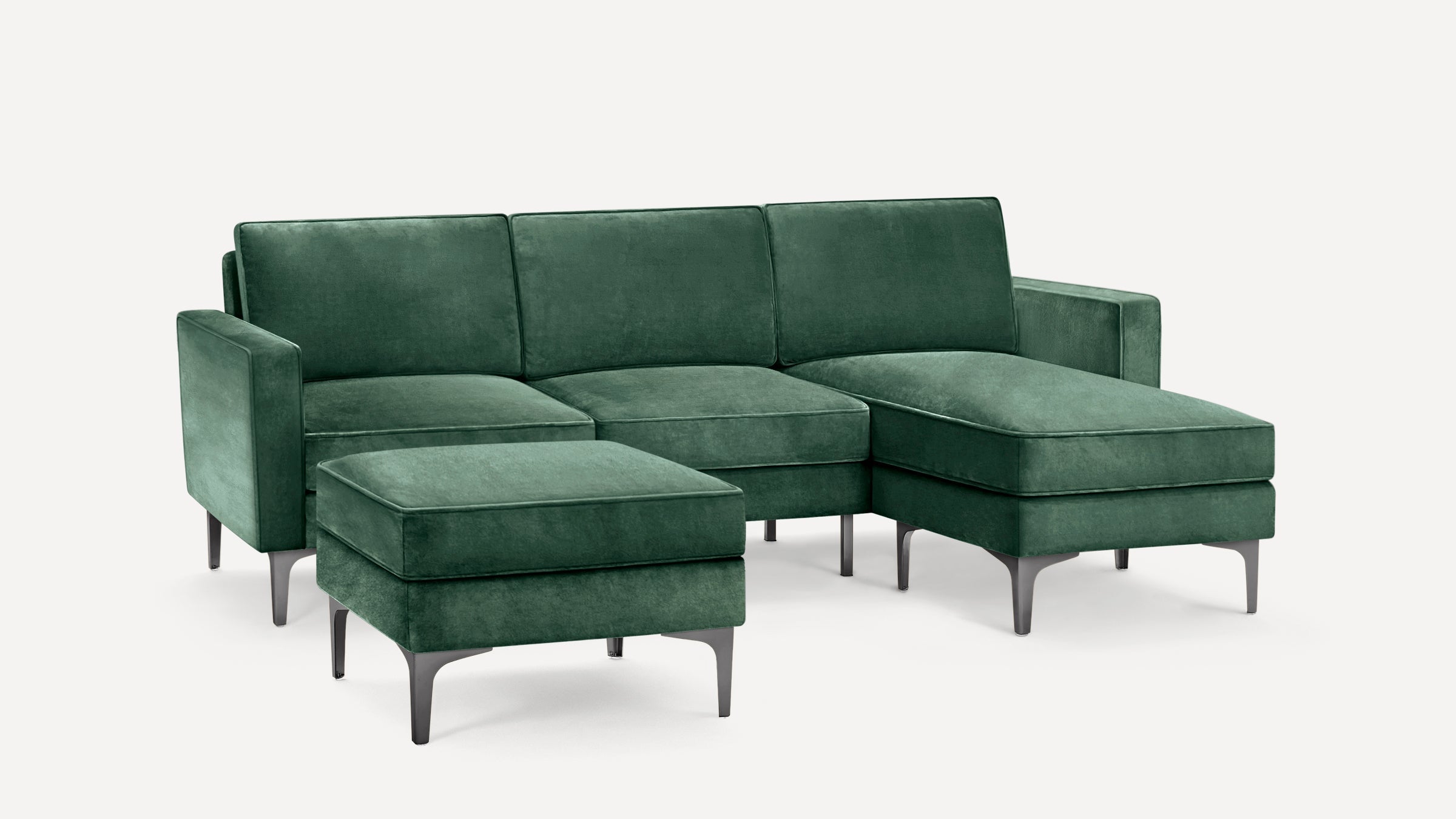 Green velvet sectional sofa with matching ottoman, sleek metal legs, and modern design on a white background.
