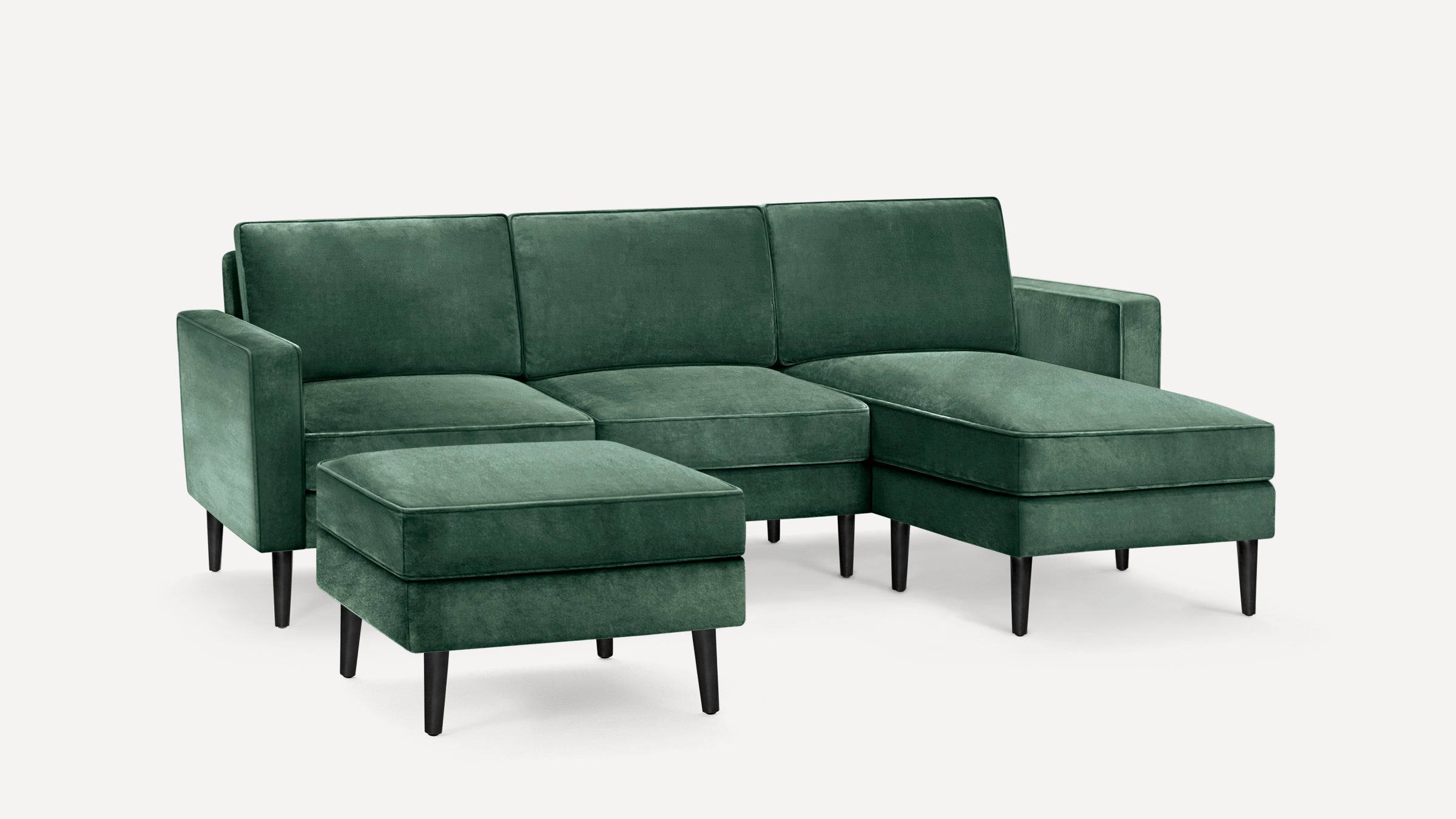 Green velvet sectional sofa with chaise lounge and matching ottoman, featuring black tapered wooden legs and clean modern lines.