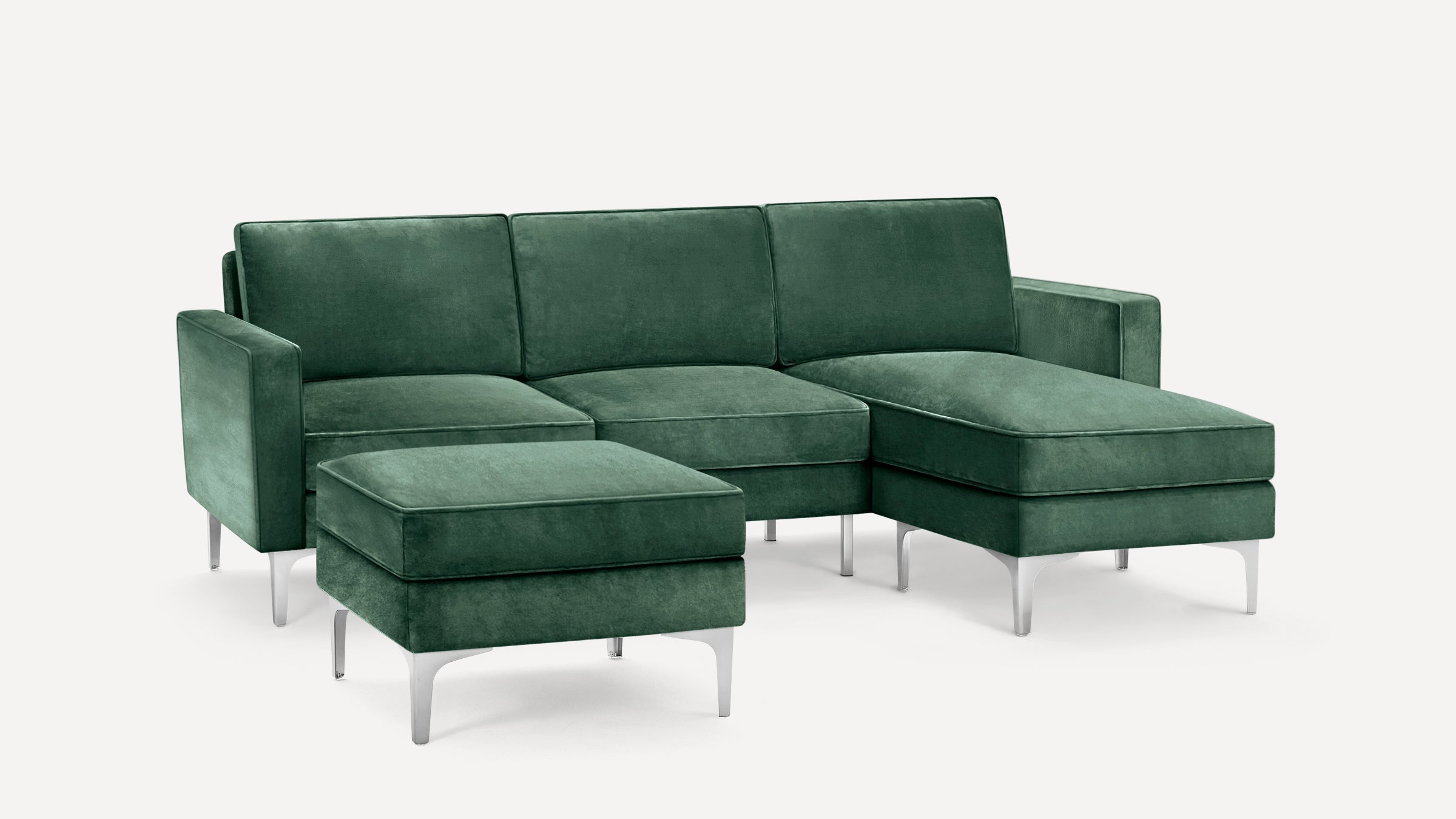 Modern green velvet sectional sofa with silver metal legs, featuring a chaise lounge and matching ottoman.