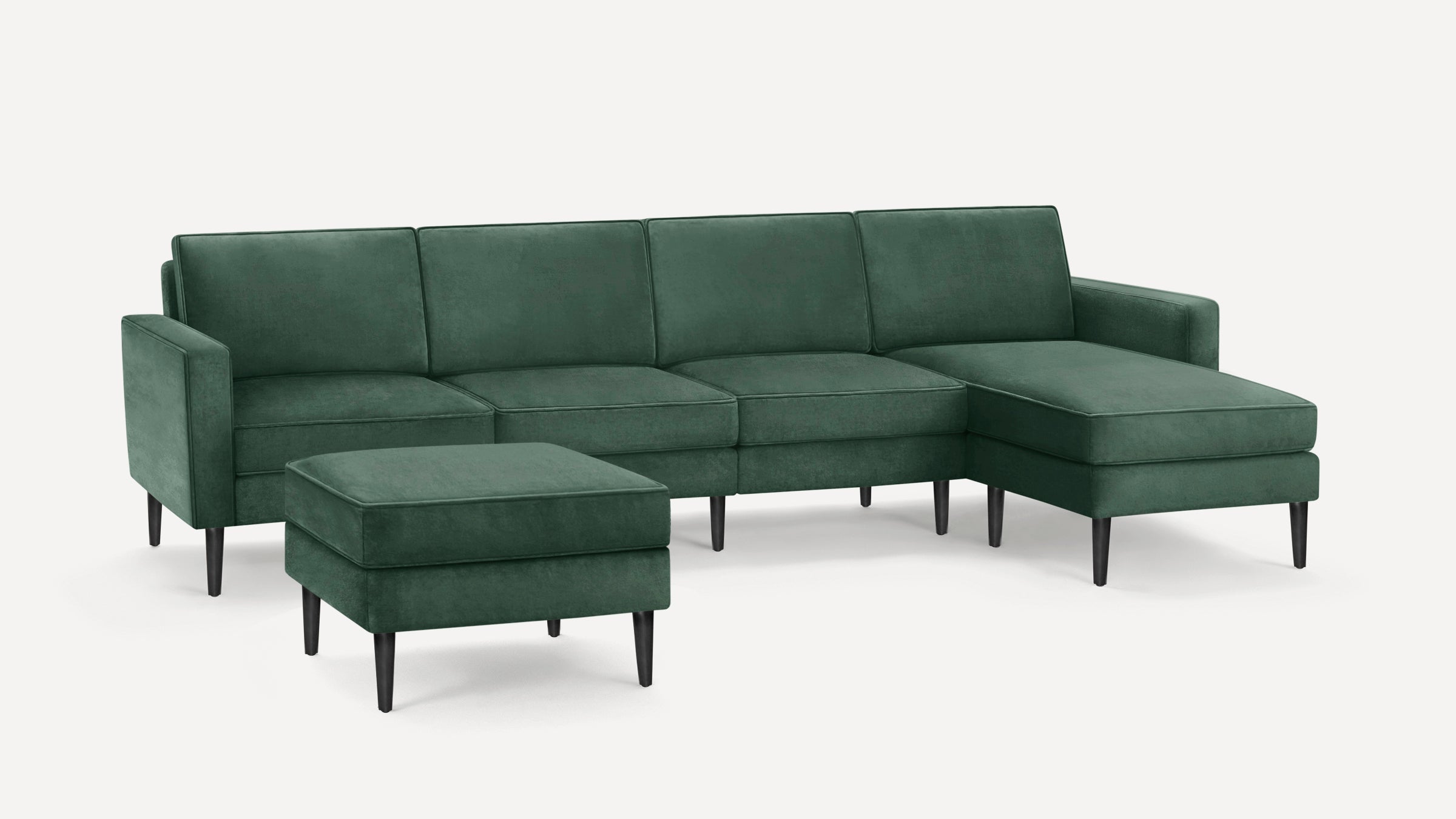 Deep green velvet sectional sofa with chaise lounge and matching ottoman, featuring slender black legs and clean modern lines.
