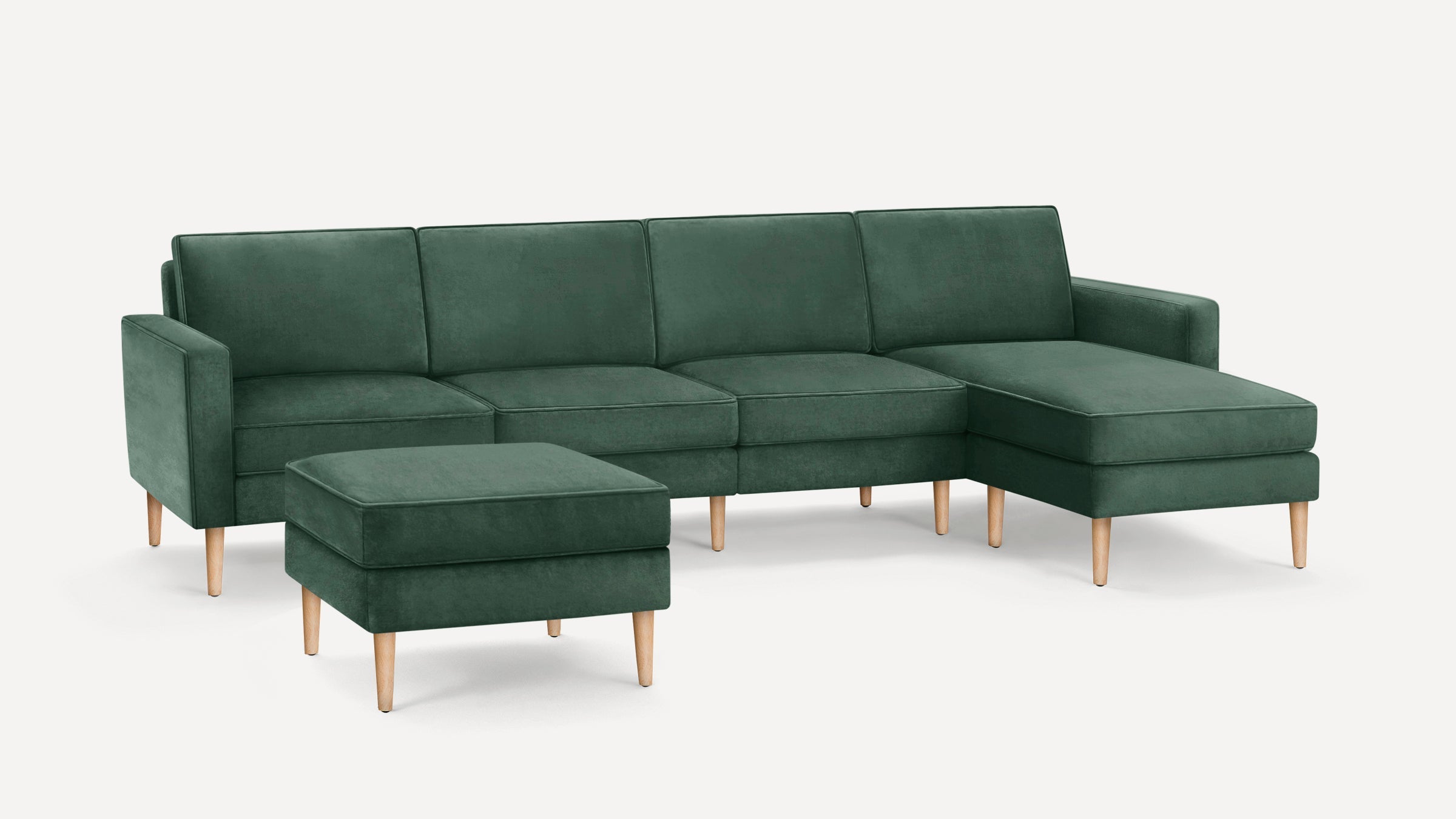 Green velvet sectional sofa with wooden legs and matching square ottoman, featuring clean lines and modern design.