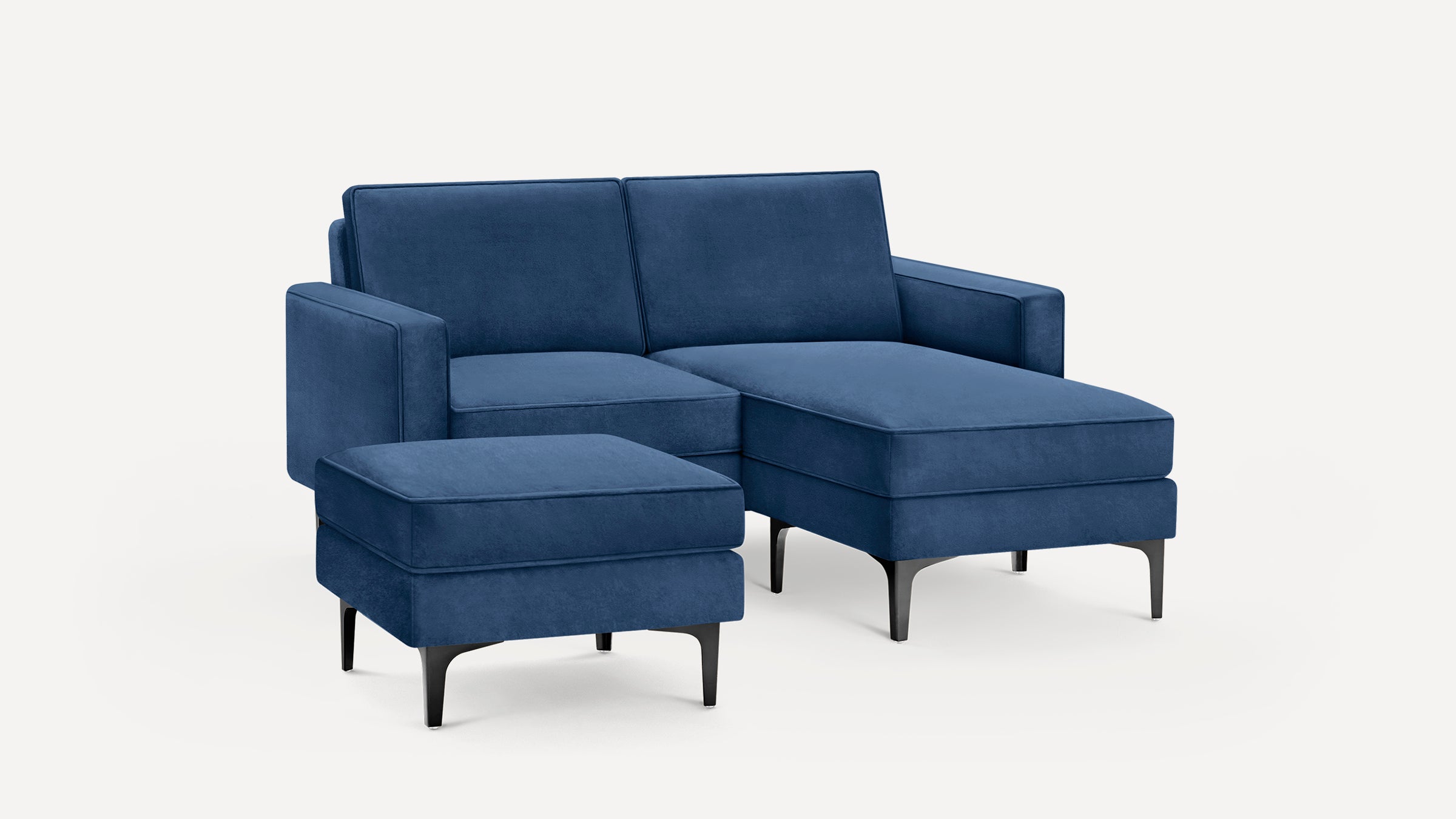 Modern blue velvet sectional sofa with chaise lounge and matching ottoman, featuring black tapered legs and clean lines.