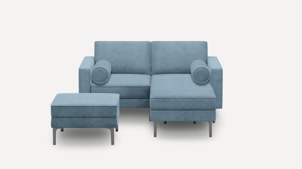 Modern blue fabric sectional sofa with a matching ottoman, metal legs, and two cylindrical accent pillows on a light background.