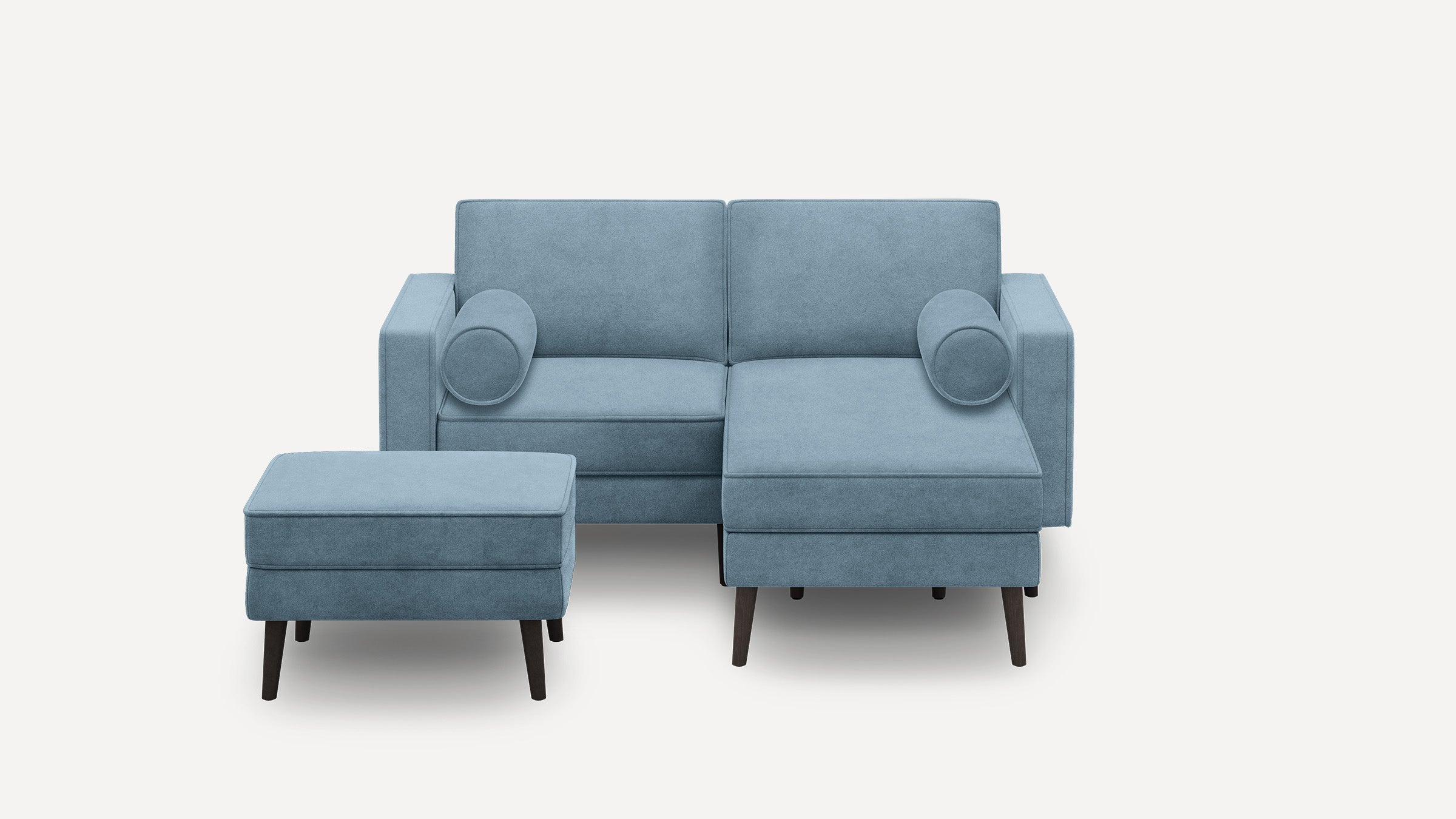 Light blue upholstered modern sectional sofa with matching ottoman and cylindrical bolster pillows on wooden legs.