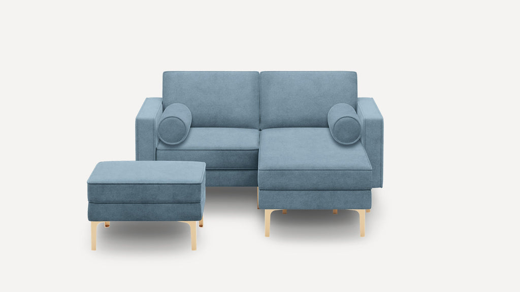 Blue upholstered sectional sofa with matching ottoman, wooden legs, and two cylindrical side pillows on a white background.