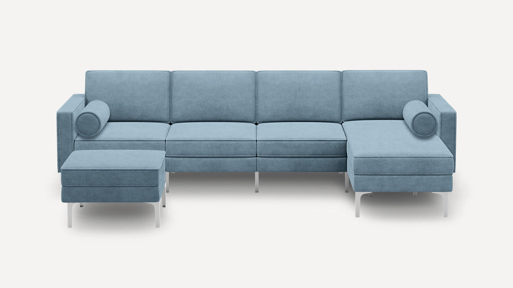 Modern light blue sectional sofa with clean lines, metal legs, two cylindrical bolster pillows, and an ottoman on the left side.