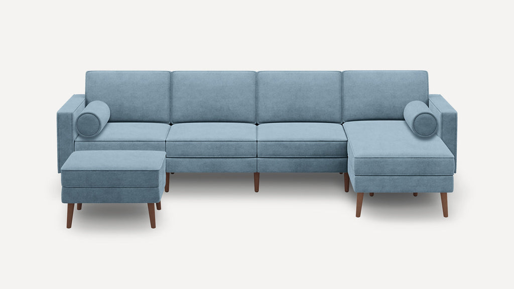 Light blue modular sectional sofa with wooden legs, including a chaise lounge, ottoman, and cylindrical bolster pillows on each end.
