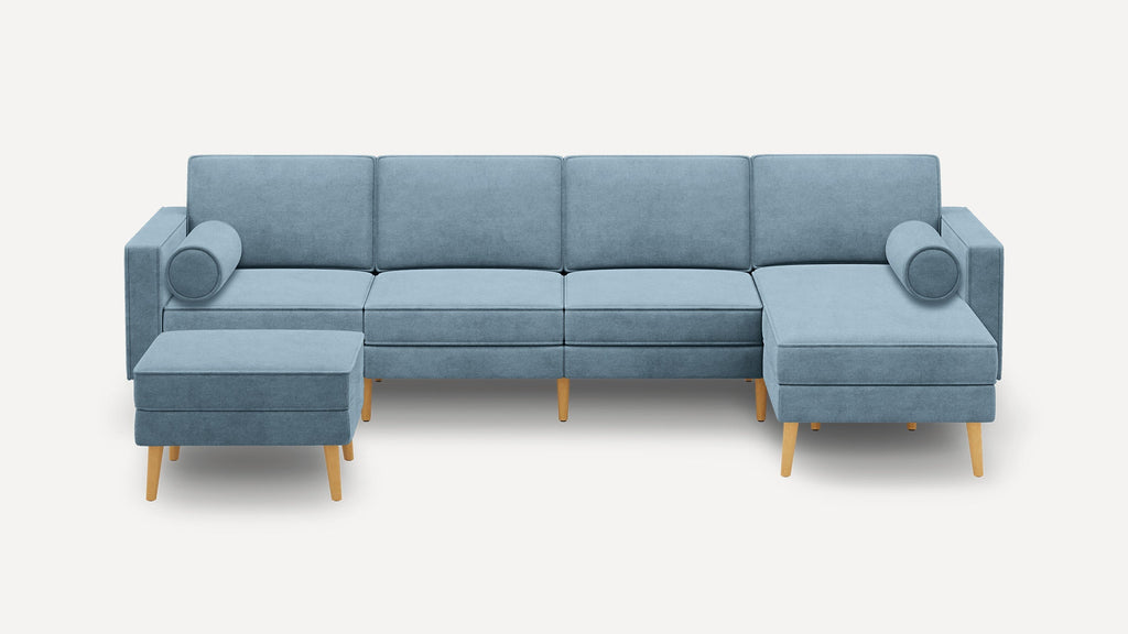 Light blue sectional sofa with wooden legs, includes two cylindrical bolster pillows and a matching ottoman.