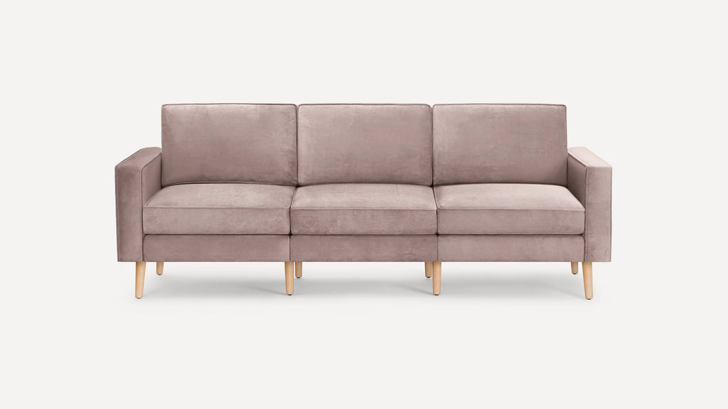 Three-seat modern sofa in muted pink fabric with straight arms and light wooden legs on white background.