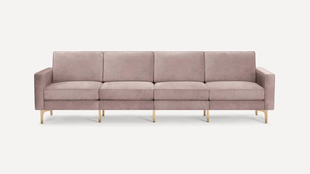 Four-seater modern sofa with blush pink velvet upholstery and sleek gold metal legs on white background.