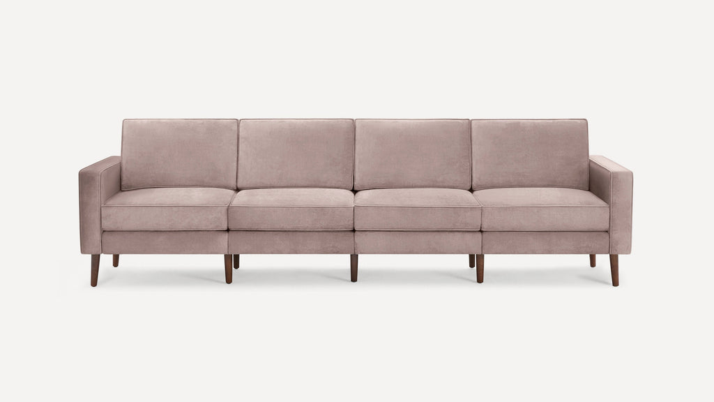 Modern four-seater sofa upholstered in soft blush pink fabric with clean lines and tapered wooden legs.