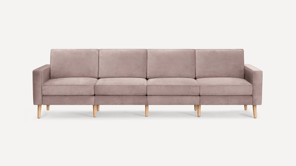 Modern four-seat sofa with soft mauve upholstery and light wooden legs, featuring clean lines and padded armrests.
