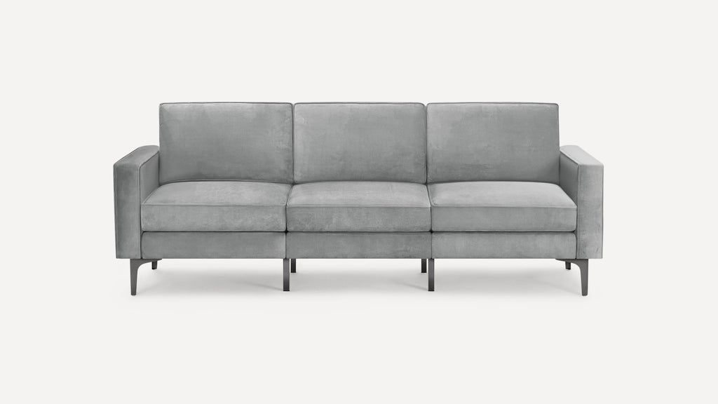 Modern three-seater sofa upholstered in light gray velvet fabric with slim metal legs and clean lines.
