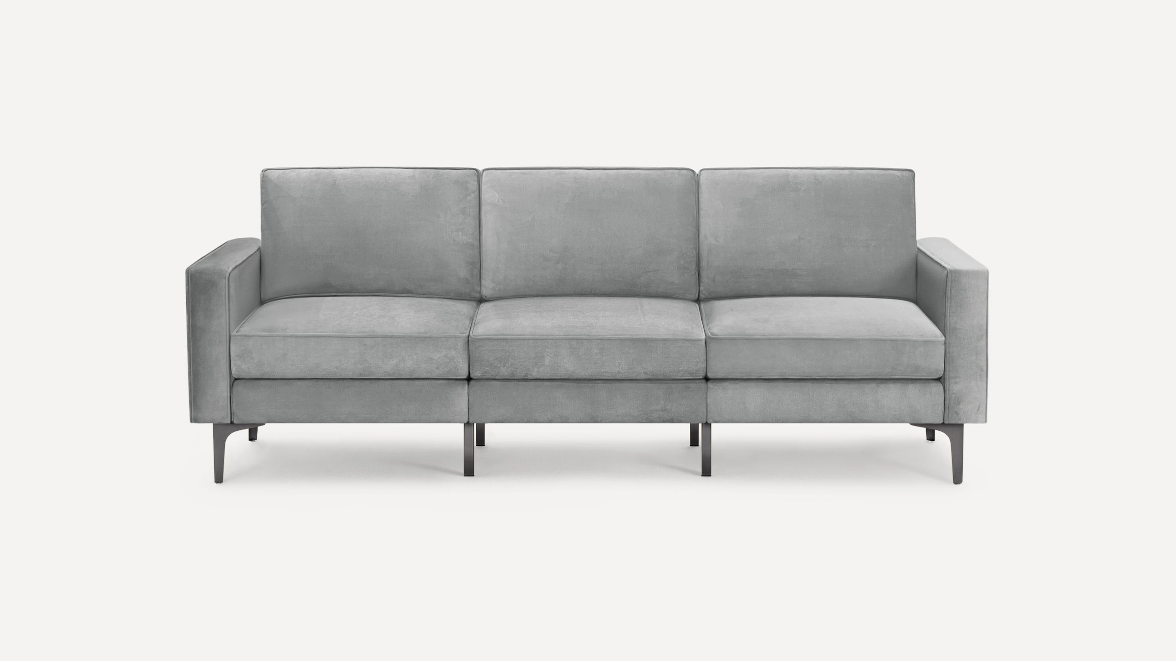 Modern three-seater sofa upholstered in light gray velvet fabric with slim metal legs and clean lines.