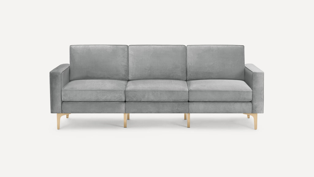 Modern three-seat sofa with light grey velvet upholstery and gold-tone metal legs on a white background.