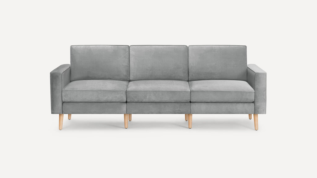 Modern three-seater sofa upholstered in soft gray fabric with straight arms and light wooden legs on a white background.