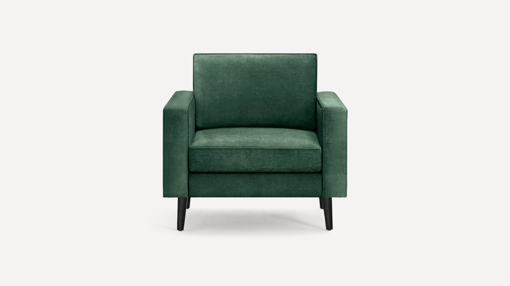 Modern green velvet upholstered armchair with clean lines and tapered black wooden legs against white background.