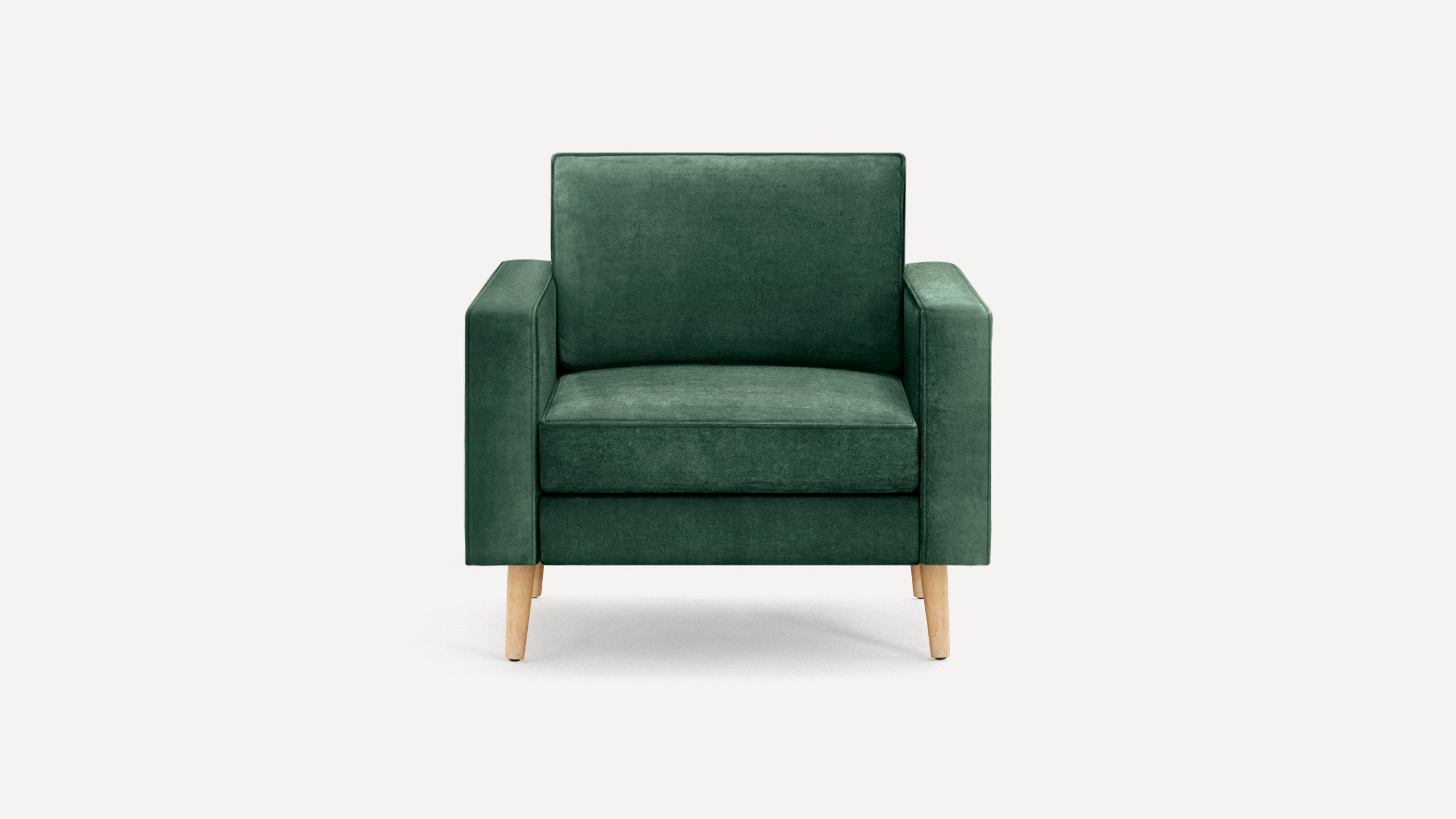 Dark green velvet armchair with wooden legs, featuring a boxy design and cushioned seat and backrest.