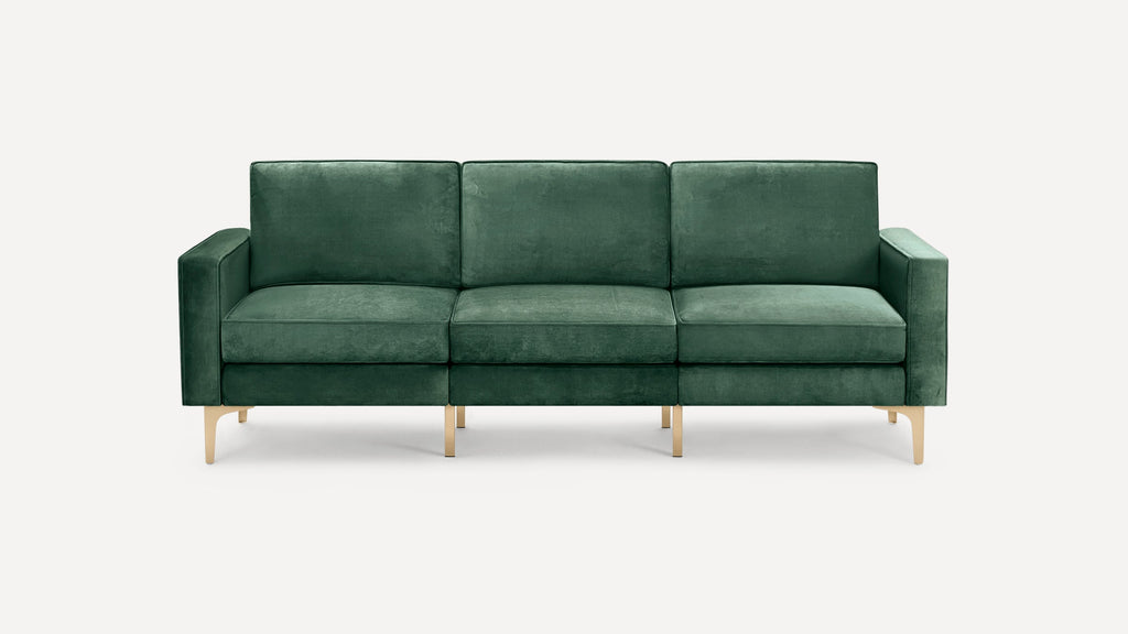 Modern three-seat sofa upholstered in deep green velvet fabric with clean lines and slender gold metal legs, set against a plain light background.