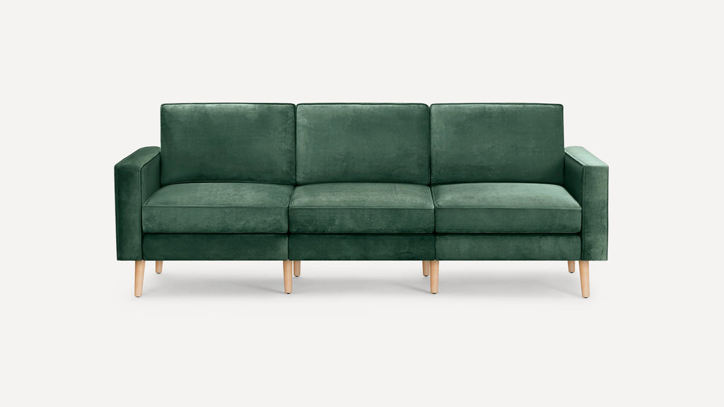 Modern three-seater sofa with deep green velvet upholstery and light wooden tapered legs, featuring clean lines and square armrests.