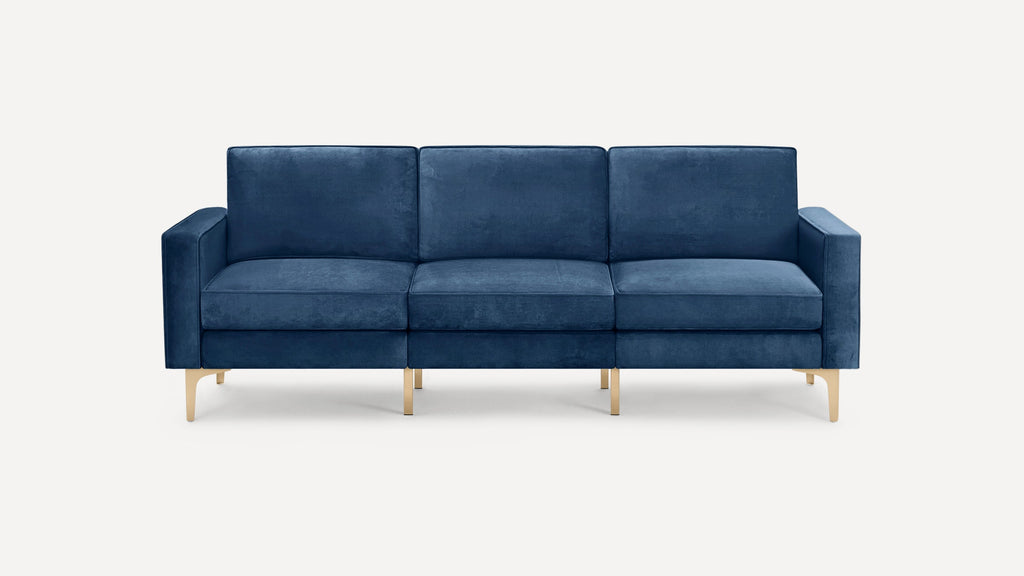 Modern navy blue velvet sofa with three seat cushions, square arms, and sleek gold metal legs, set against a white background.