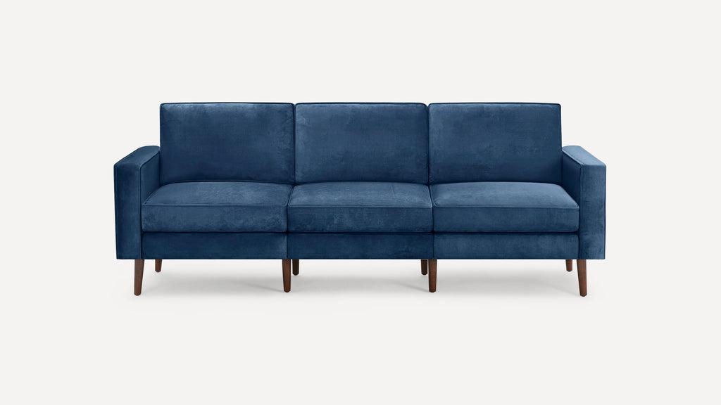 Modern navy blue three-seater sofa with plush cushions, straight arms, and wooden tapered legs on a white background.