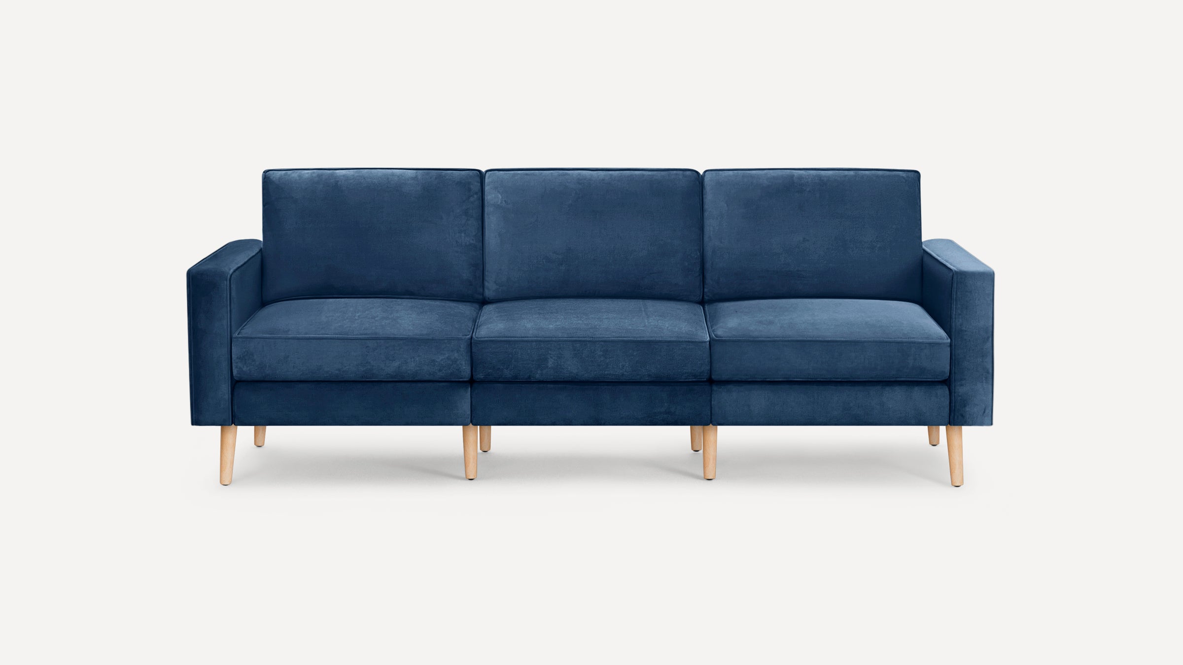 Modern three-seater sofa upholstered in deep blue velvet fabric with light wooden tapered legs and square armrests, set against a plain white background.