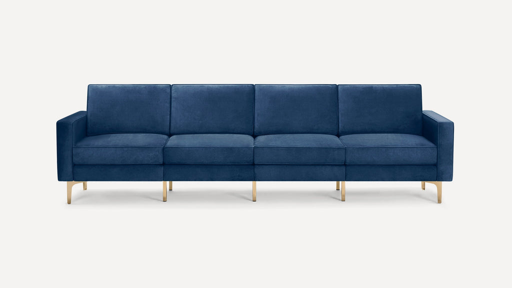 Modern four-seater sofa upholstered in deep blue velvet with clean lines and gold metal legs, against a white background.