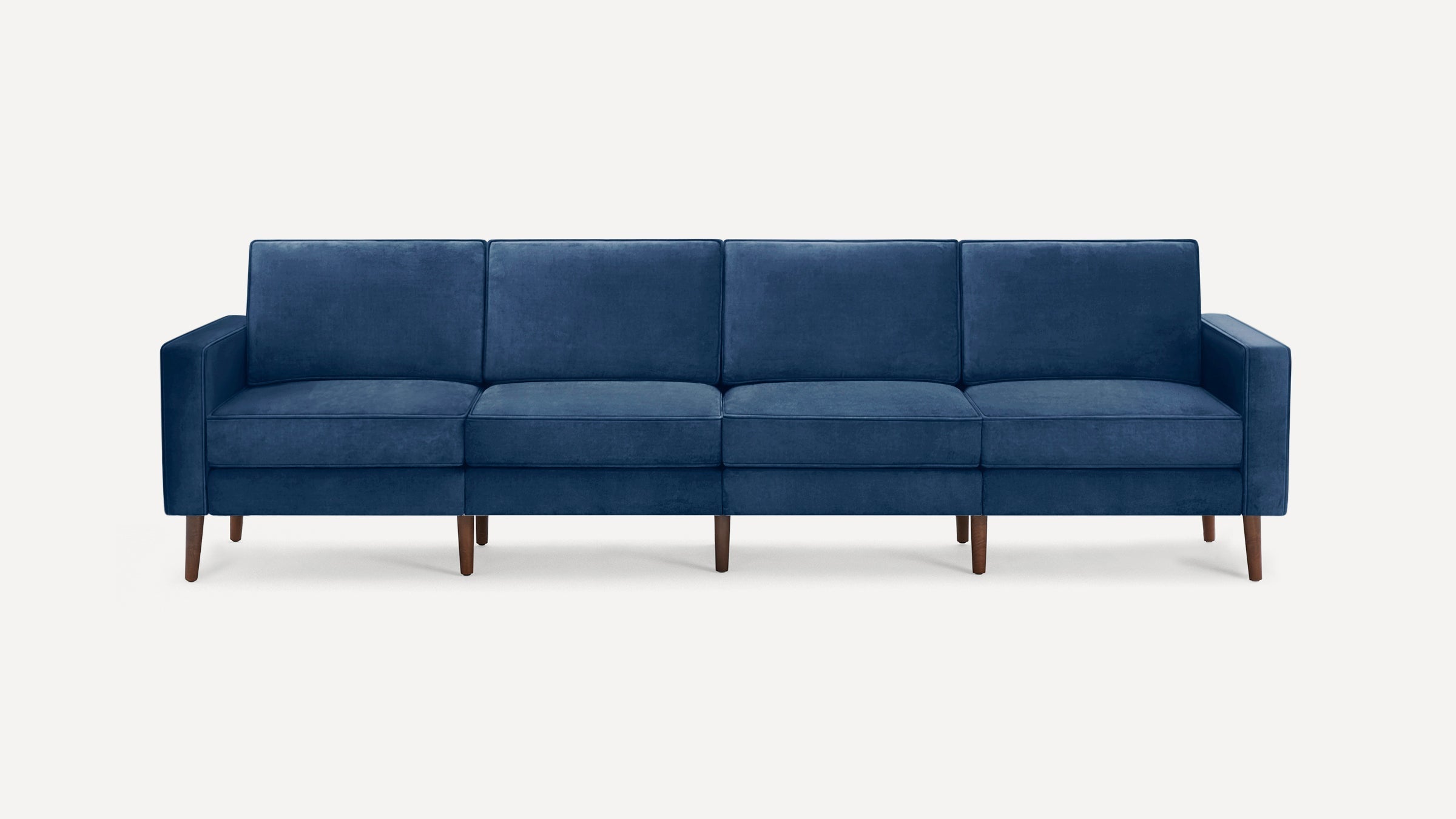 Four-seater modern sofa with deep blue velvet upholstery and wooden tapered legs against a plain background.